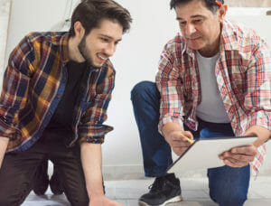 Two middle age men kneeling down looking at a clipboard